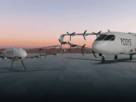 Two electric aircraft with multiple propellers parked on a runway at sunset.