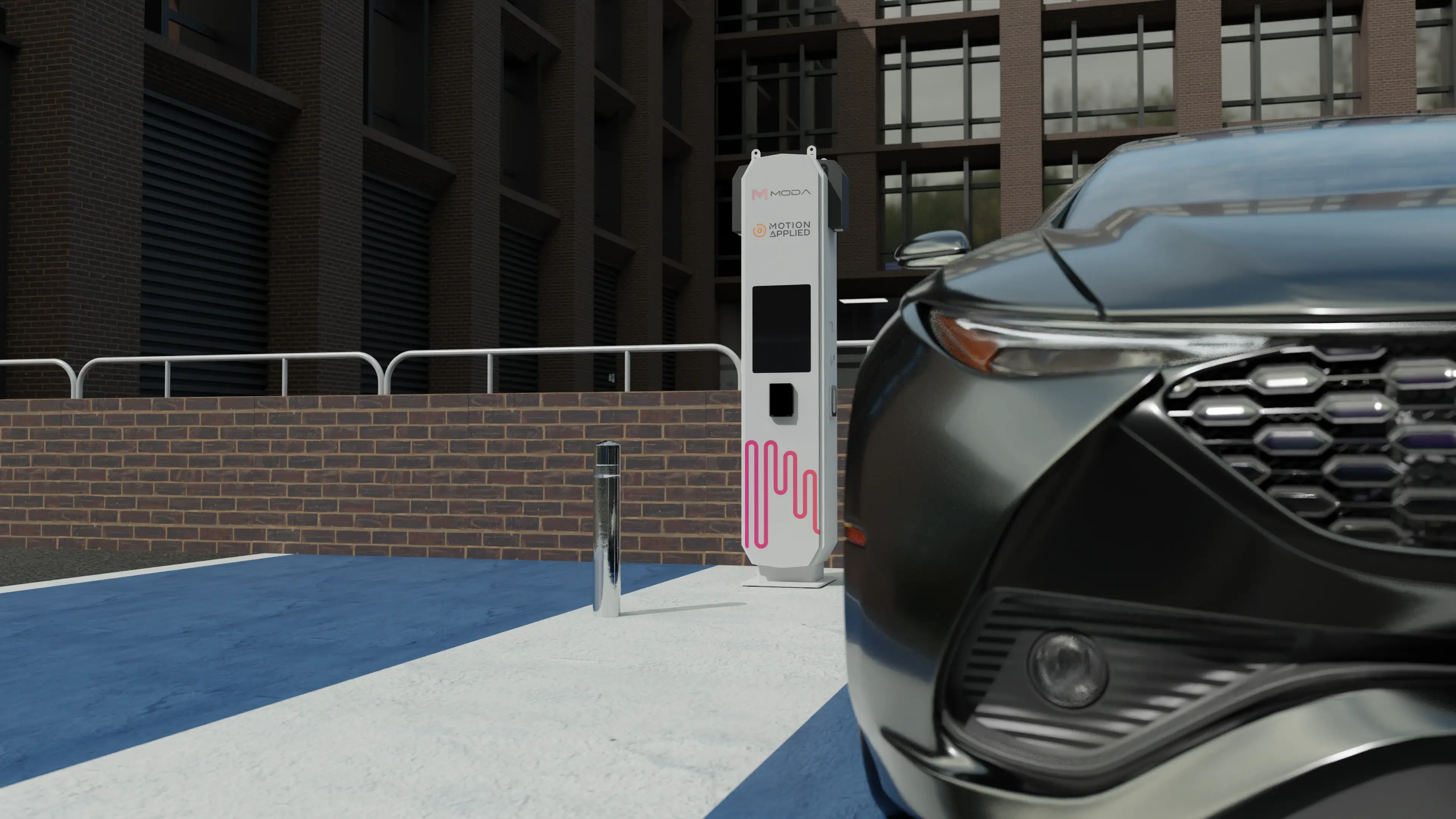 Urban street scene showing the front of a dark car parked beside a Motion Applied vehicle charging station, with the charger unit visible against a modern brick building.